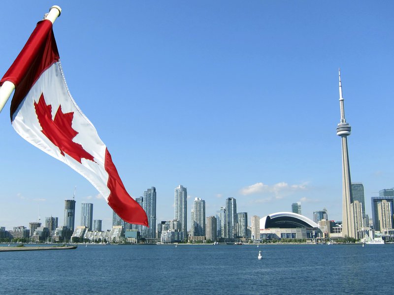 A Canadian flag flutters, with the Toronto skyline in the background